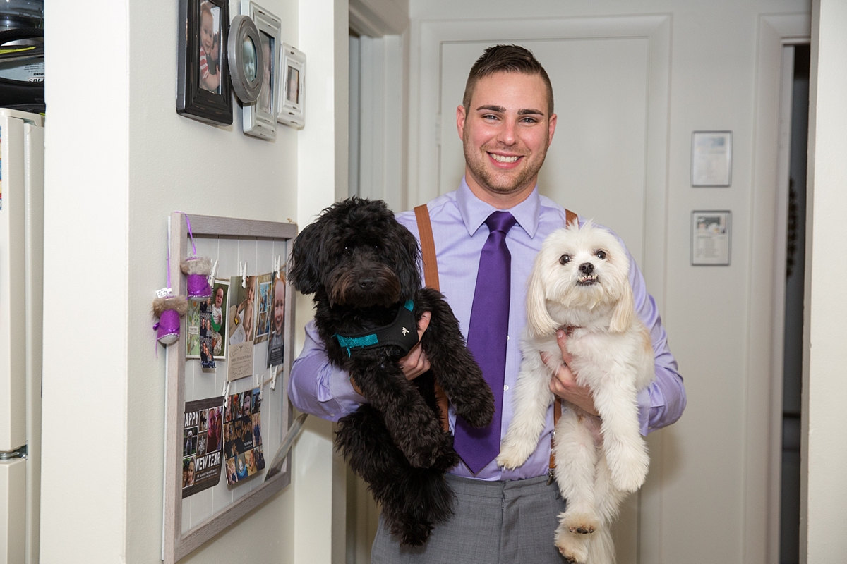 groom in purple tie poses with his dogs